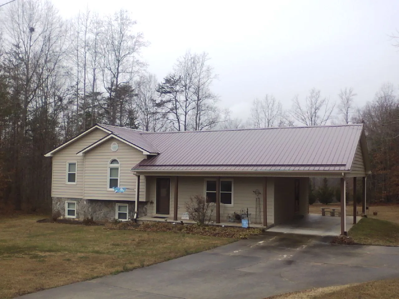 Burgundy metal roof on a tan split level home with an attached carport in Osage