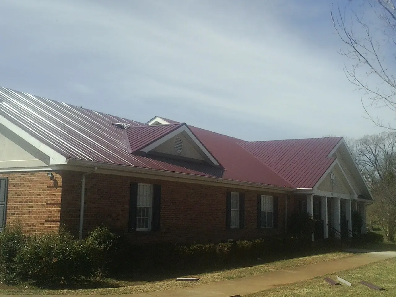Red metal roof with gabled entries on a long brick building, from a Hail Damage Roof Repair job in Osage