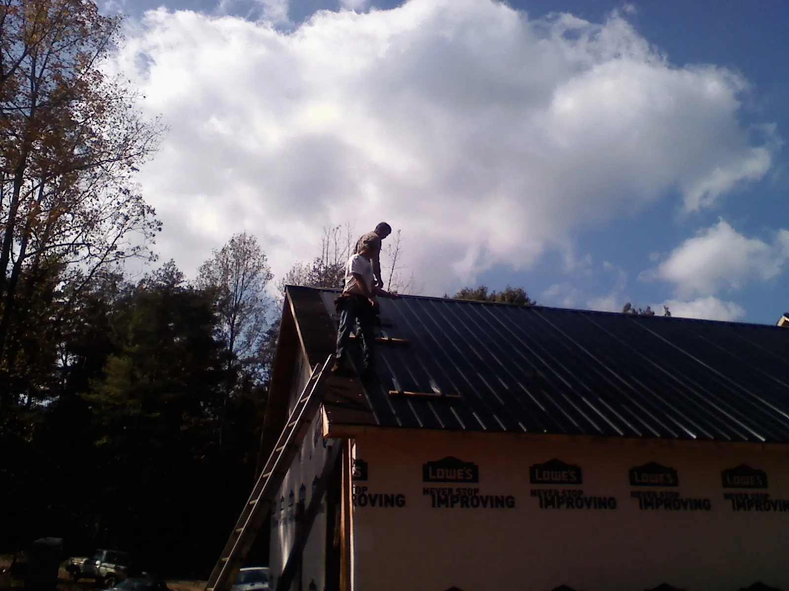 Roofer fastening dark metal panels high against a cloudy sky, from a Roof Inspection job in Osage