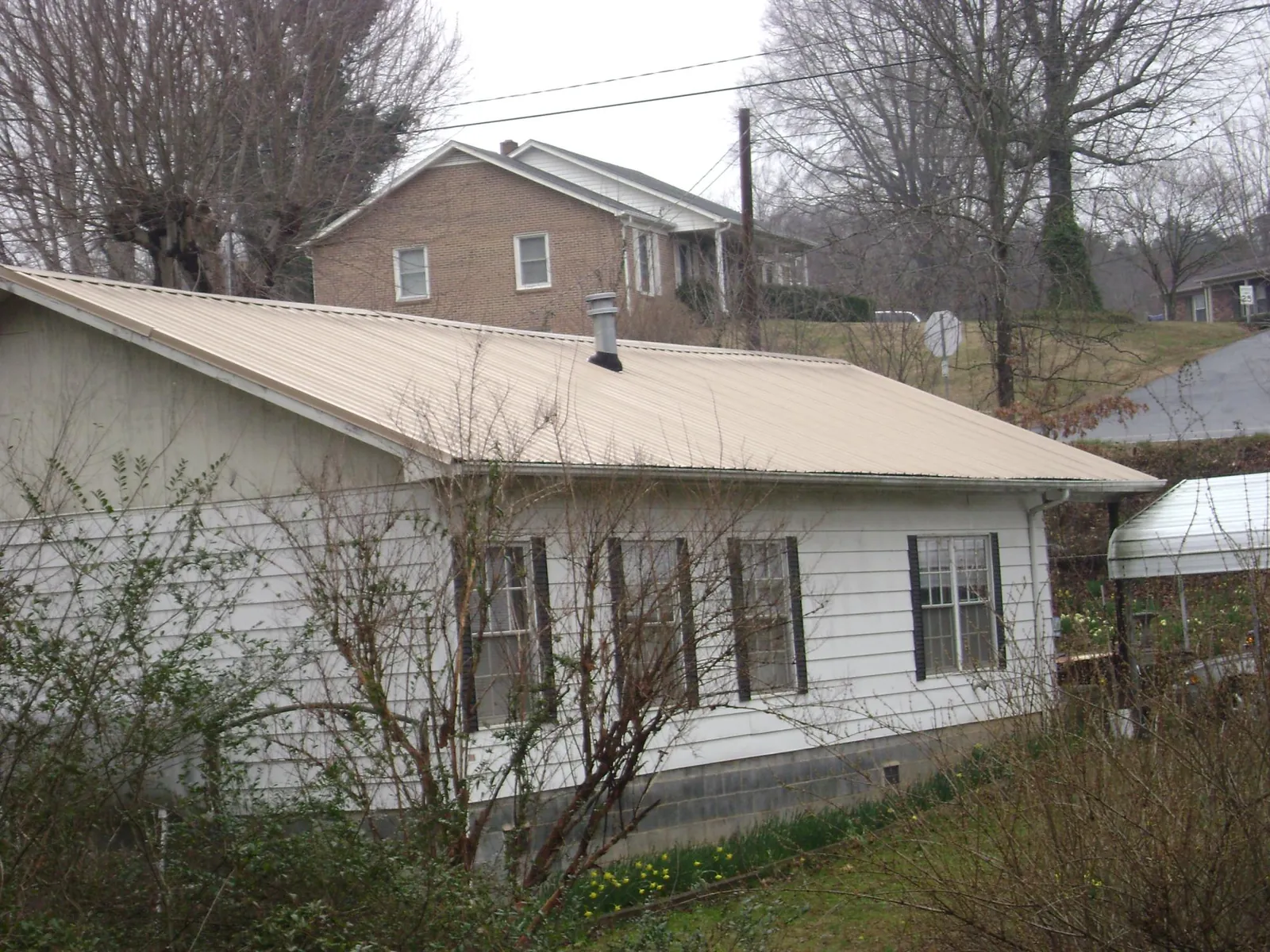 Tan metal roof on a white sided house set into a hillside — Commercial Roofing by Roofing Brothers in Osage