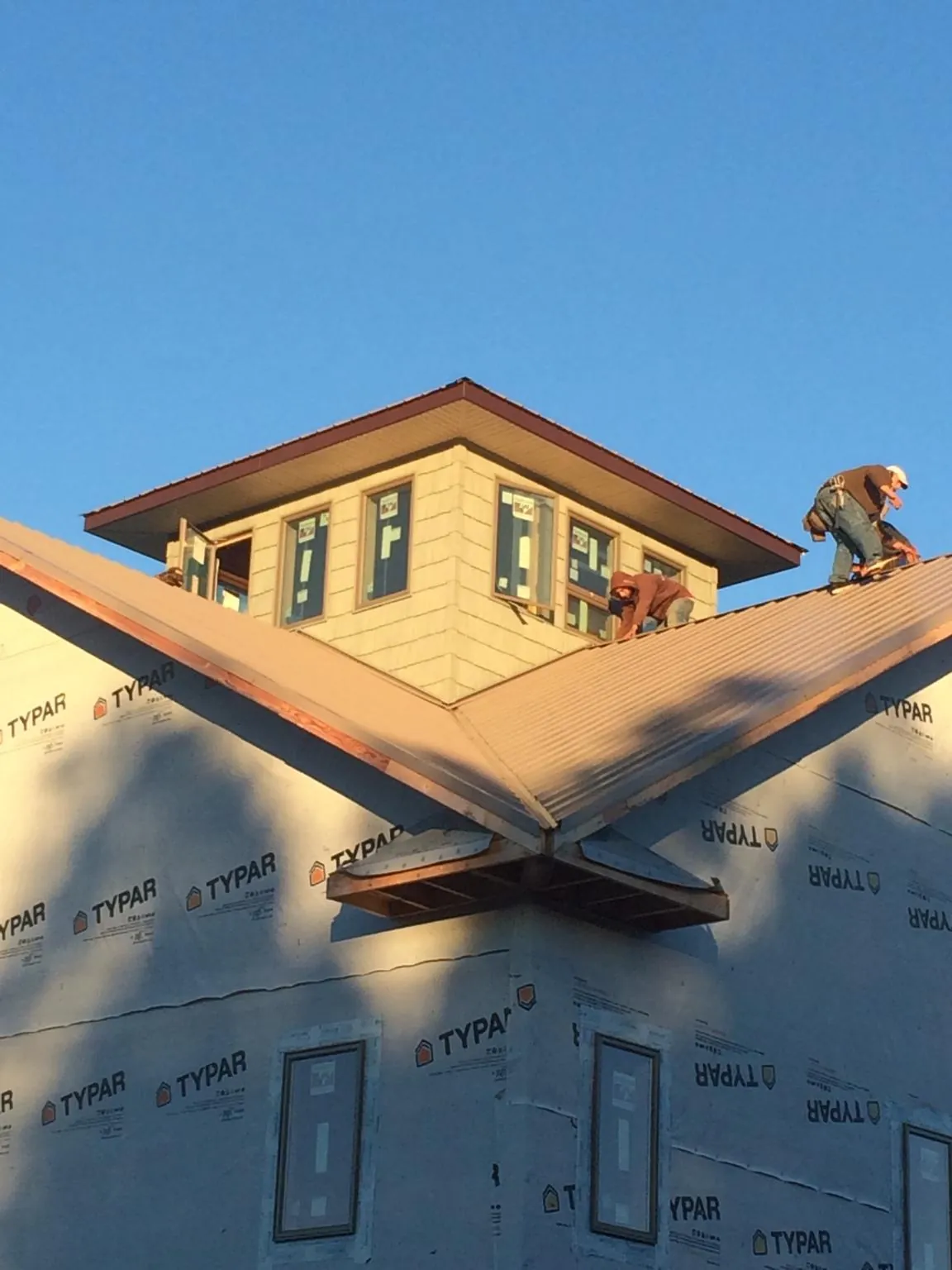 Roofers working around a rooftop cupola on a new metal roof at sunset — Roof Waterproofing in Osage by Roofing Brothers
